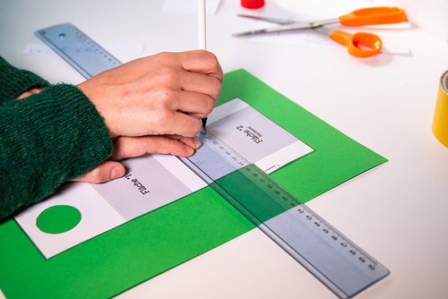 Man sieht eine Person, die mit einem Lineal Markierungen auf grünem Bastelkarton macht