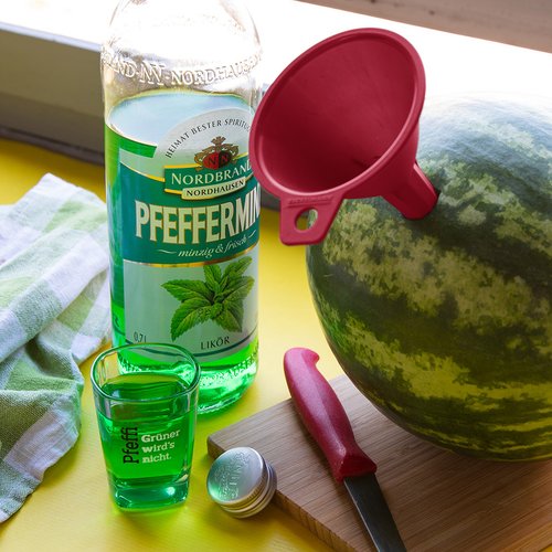 Man sieht eine Melone, in die ein Trichter gesteckt wurde nebst Pfeffi Flasche