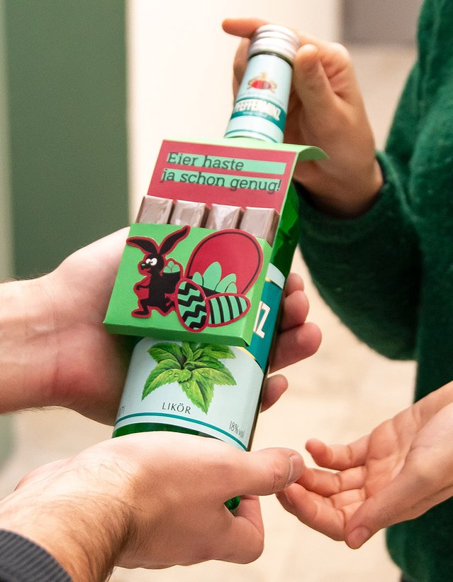 Das Bild zeigt, wie eine Pfeffi Flasche, mit einem Anhänger im Pfeffi Style, in dem sich Süßigkeiten befinden, den Besitzer wechselt