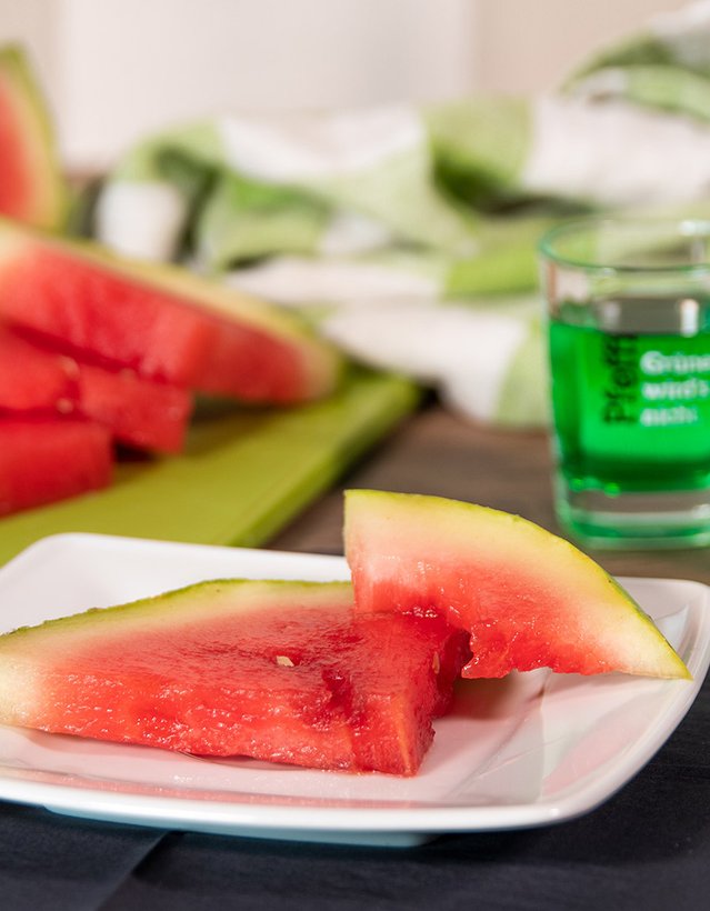 Man sieht eine angeschnittene Wassermelone auf einem Teller nebst Pfeffi Pinnchen