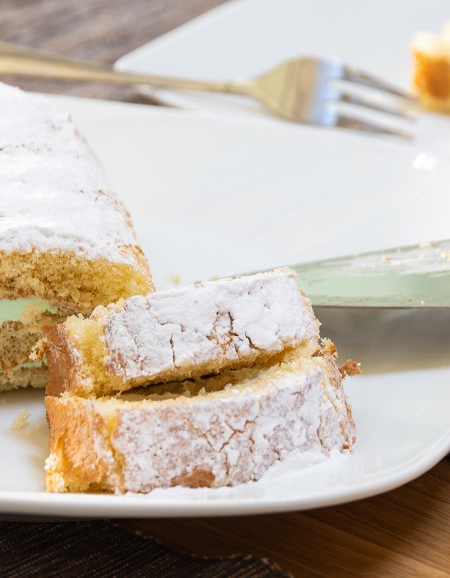 Das Bild zeigt einen angeschnittenen Kuchen mit grünlicher Füllung auf einem Teller