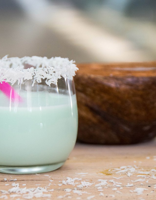 Das Bild zeigt einen Cocktail mit Kokosflockenrand vor einer Kokosnuss