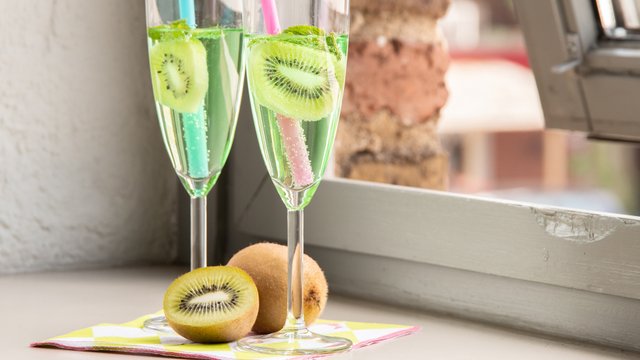Das Bild zeigt einen Pfeffi Cocktail in Sektgläsern mit Kiwi-Scheibe auf einer Fensterbank.