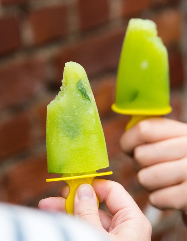 Das Bild zeigt eine Hand, die ein grün-gelbes Eis am Stil vor sich hält