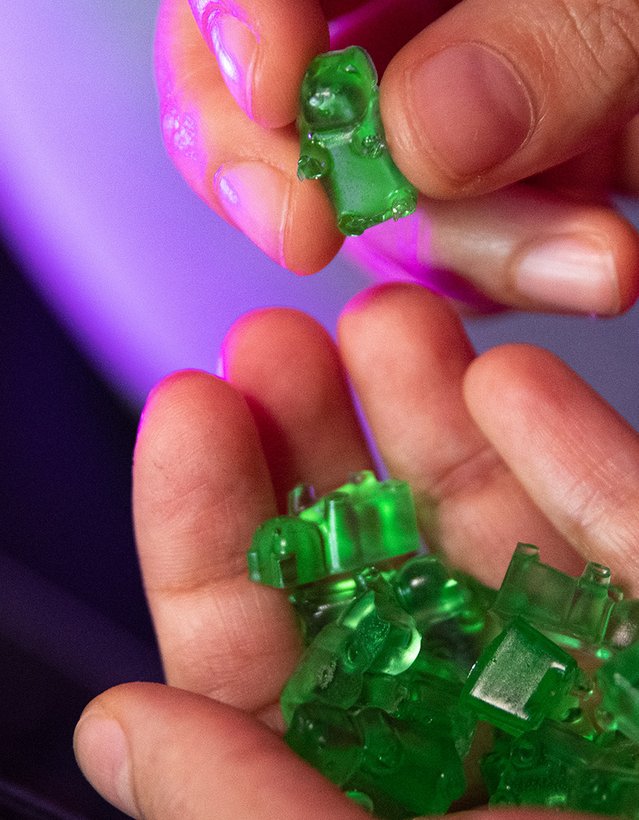 Man sieht eine Hand mit grünen Gummibärchen darin. Im Hintergrund ist eine Fernbedienung zu sehen
