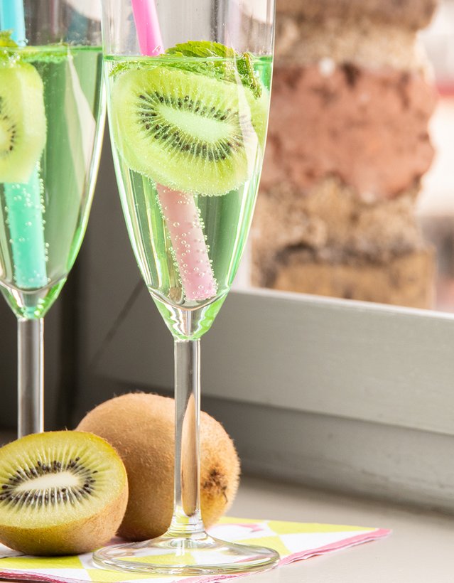 Das Bild zeigt einen Pfeffi Cocktail in Sektgläsern mit Kiwi-Scheibe auf einer Fensterbank.