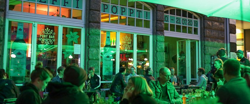 Man sieht den Pfeffi Pop-up-Store in Hamburg von außen, viele Menschen sitzen davor, alles ist in grünes Licht getraucht