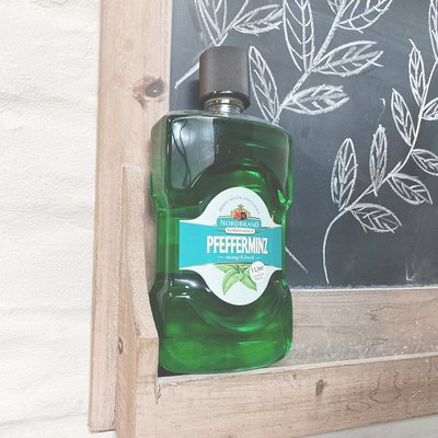 Mundwasser Fanbild 2 Das Bild zeigt eine Mundwasser Flasche neben einer Tafeln auf die ein florales Muster mit Kreide gemalt wurde