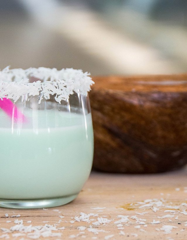 Das Bild zeigt einen Cocktail mit Kokosflockenrand vor einer Kokosnuss