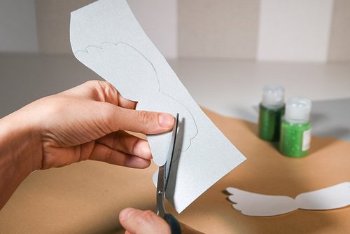 Das Bild zeigt, wie aus silbernen Karton Flügel ausgeschnitten werden