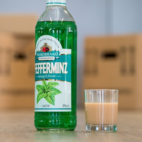 Man sieht eine Flasche Pfeffi nebst einer milchig-bräunlichen Flüssigkeit