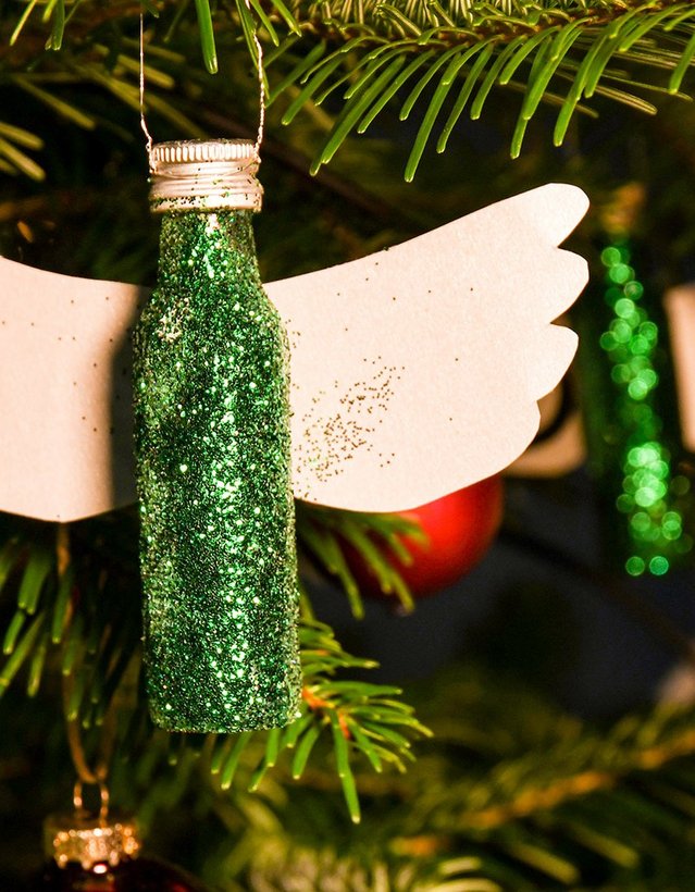 Das Bild zeigt eine mit grünem Glitzer bedeckte Pfeffi Mini Flasche, die mit zwei Flügeln an der Rückseite versehen wurde, sodass sie wie eine Engelsfigur aussieht. Sie hängt an einem Christbaum.
