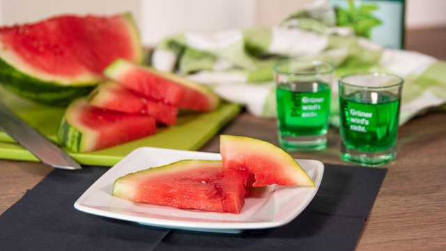 Man sieht eine angeschnittene Wassermelone auf einem Teller nebst Pfeffi Pinnchen