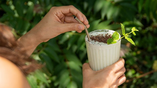 Das Bild zeigt eine Hand, die einen Milchshake mit einem Minzzweig hält