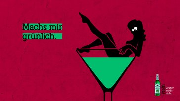 Das Bild zeigt eine schwarze Frau, die in einem riesigen Martiniglas mit grüner Flüssigkeit badet vor rotem Hintergrund