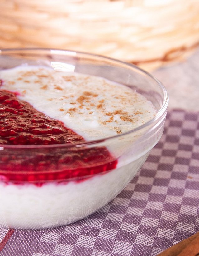 Pfeffi Rezept Milchreis Das Bild zeigt eine Schale Milchreis mit Beerenkompott auf einem Geschirrhandtuch nebst Zimtstange
