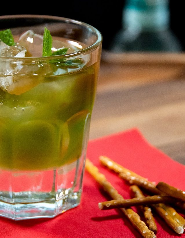 Pfeffi Rezept Knallfrosch Das Bild zeigt einen grünen Pfeffi Cocktail auf einer roten Serviette nebst Salzstangen