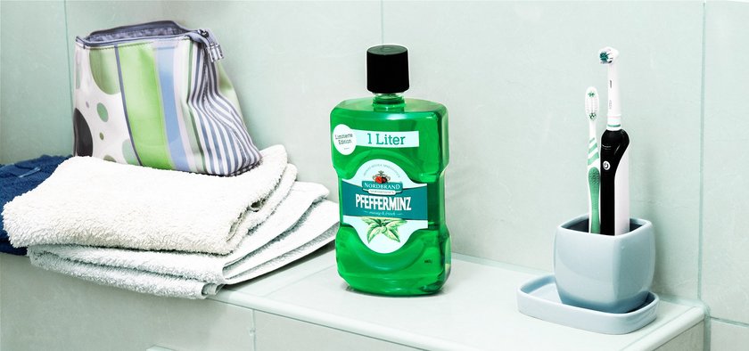 Pfeffi Mundwasser Bad Das Bild zeigt eine Pfeffi Mundwasser Flasche in einem Bad nebst Zahnbürste und diversen Handtüchern.