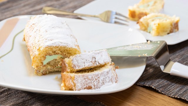 Das Bild zeigt einen angeschnittenen Kuchen mit grünlicher Füllung auf einem Teller