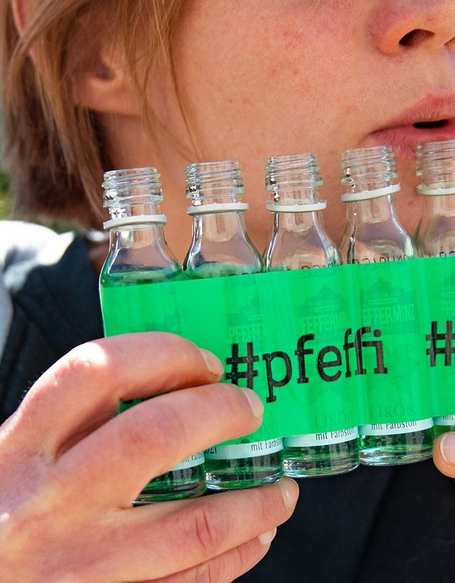 DIY: Pfeffi Panflöte Das Bild zeigt mehrere Pfeffi Mini Flaschen, die mit Klebeband in einer Reihe zusammengeklebt sind. Eine Person scheint darauf, wie auf einer Panflöte zu spielen.
