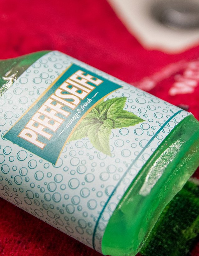 Das Bild zeigt eine grüne Seife in Pfeffi Flaschenform mit einer Banderole, auf der "Pfeffiseife" steht.