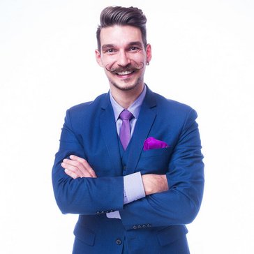 Das Bild zeigt einen lachenden Mann im Anzug mit gezwirbeltem Schnurrbart