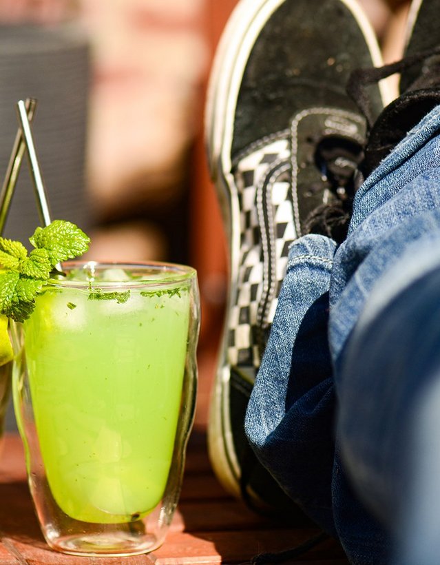 Das Bild zeigt zwei grüne Cocktails auf einem Gartentisch, daneben hochgelegte Beine