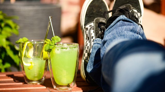 Das Bild zeigt zwei grüne Cocktails auf einem Gartentisch, daneben hochgelegte Beine