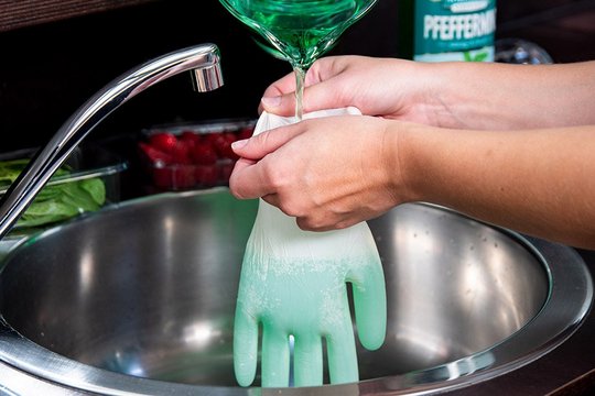 Das Bild zeigt einen Handschuh der mit einer grünen Flüssigkeit gefüllt wird