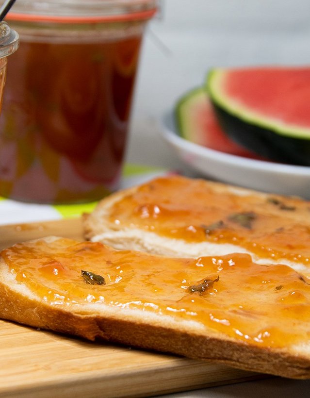 Pfeffi Rezept Konpfeffitüre Das Bild zeigt ein Marmeladenglas nebst eines mit Marmelade beschmierten Toasts, im Hintergrund liegt eine Wassermelone.