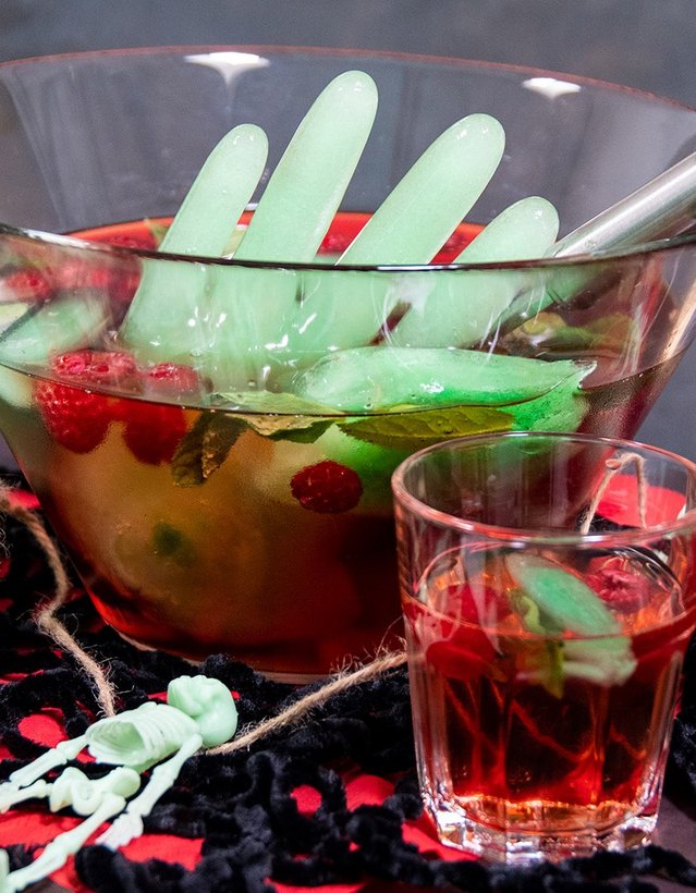 DIY: Eiskaltes Händchen Das Bild zeigt eine Bowle, die von Halloweendeko umgeben ist. Aus der Bowle ragt eine Hand aus grünem Eis